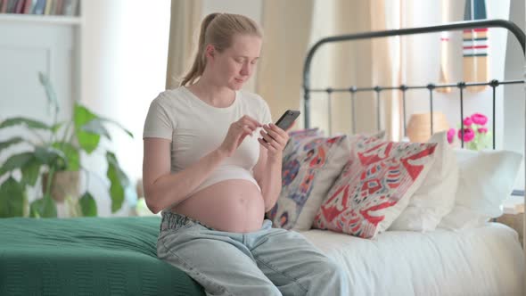 Pregnant Woman Using Smartphone While Sitting on Bed