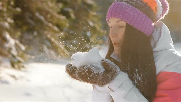 Happy Pretty Young Woman Blowing Snowflakes From Her Hands in a Winter Day