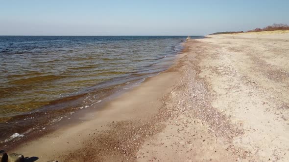 Aerial view of sea waves crashing into the beach with white sand on a sunny spring day, Baltic sea,