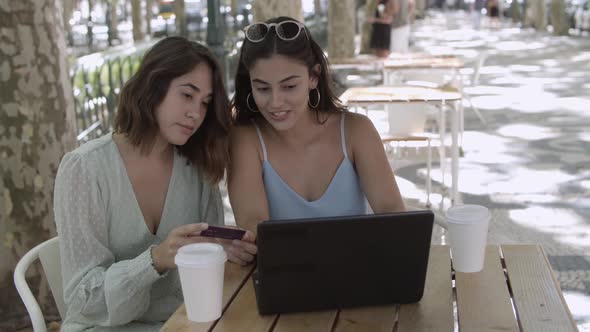 Young Female Friends Sitting in City Cafe and Using Laptop