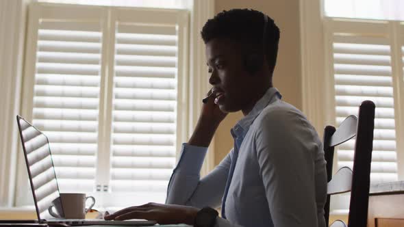 African american woman wearing phone headset having a videocall on laptop while working from home