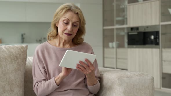 Middleaged Woman Sitting on the Sofa in the Living Room Having Fun with a Tablet Using the Concept