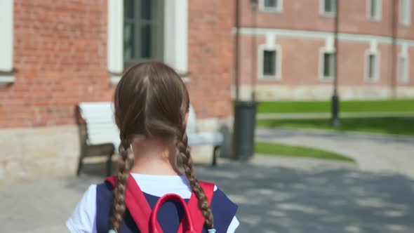 Back View of Happy Schoolgirl with Backpack Walking to School Outdoors