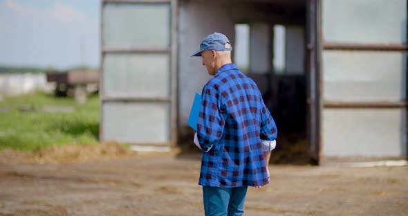 Farmer Gesturing While Writing on Clipboard Against Barn