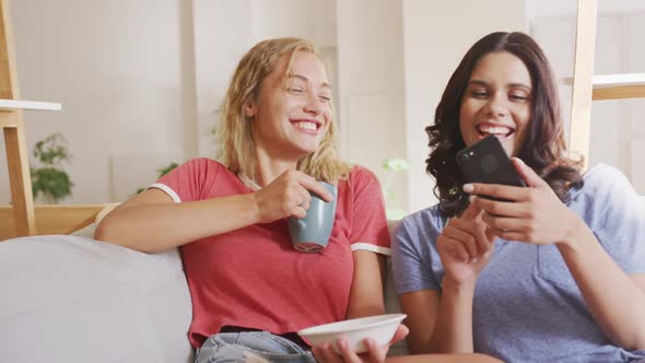 Two young woman friends laughing together while looking in a smart phone