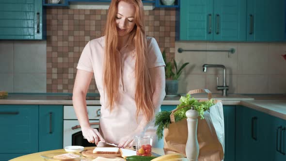 Attractive young woman in a home kitchen prepares a delicious sandwich