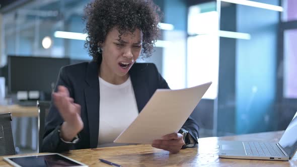 Disappointed African Businesswoman Reading Documents and Reacting To Failure with Hand Gesture