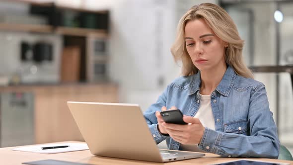 Young Woman Using Smartphone and Laptop at Work