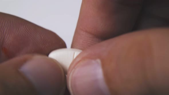 Person Breaks White Pill To Halves on Light Background Macro