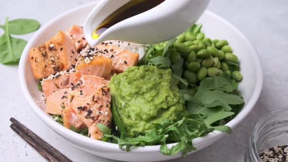 Fried salmon salad with rice, edamame and guacamole pouring soy sauce.