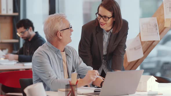 Young Female Architect Helping Senior Male Coworker in Office