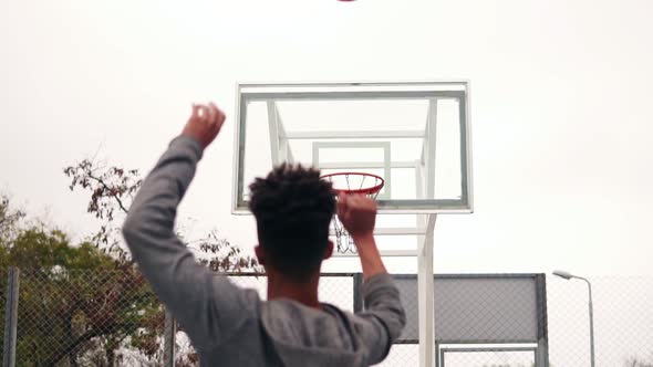 Back View of Unrecognizable African Player Jumping Up and Throwing Ball in a Basketball Hoop the