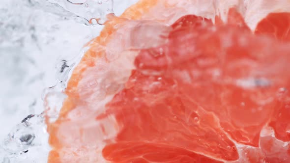 Halved pink grapefruit falling in water. Slow Motion.