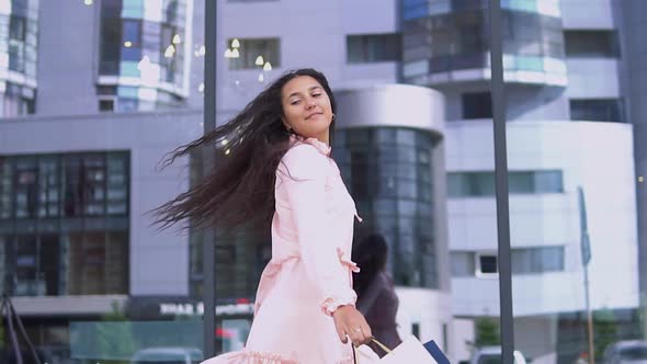 A Girl in a Dress After Shopping with Packages in Her Hands is Happy with the Purchases