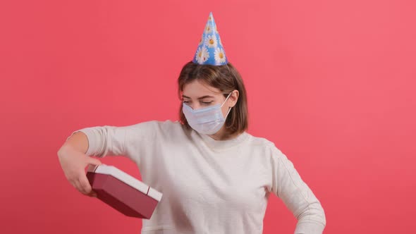 Optimistic Girl with Medical Mask on Face and Cone on Head Giving Gift Box