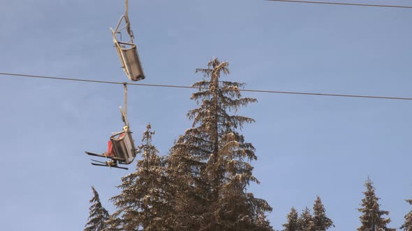 Chair Lift with Skiers in Motion on Background of Blue Sky and Snowcovered Pine Trees in Winter