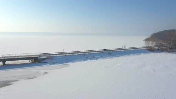 Aerial Shot of White Car Riding Through Snow Covered Road Near a Frozen Lake