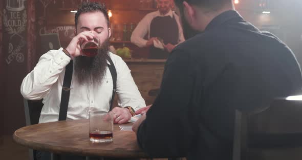 Two Bearded Men in a Bar Drinking Socializing and Start Playing a Card Game