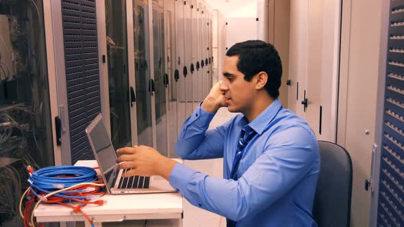 Technician talking on mobile phone in while working on laptop