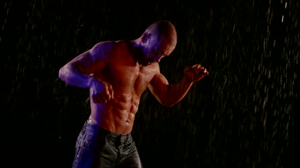 a Muscular Man with a Bare Torso is Boxing in Streams of Water on a Dark Background