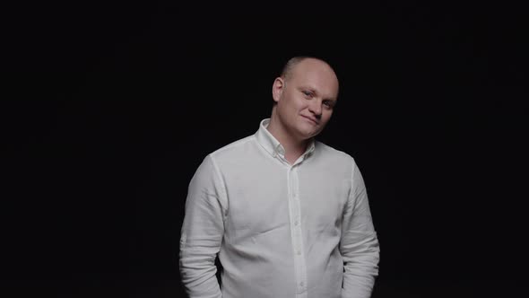 A bald man in a white shirt poses for the camera on a black background.