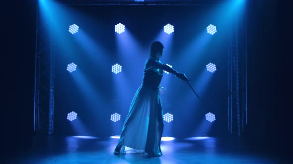 Pretty Young Woman Actress in the Image of Joan of Arc Is Dancing on Stage with a Sword. Silhouette