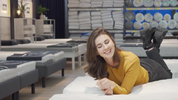 Charming Woman Lying on New Orthopedic Mattress at Furniture Store