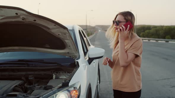 A Young Woman Makes a Phone Call Standing By a Broken Car