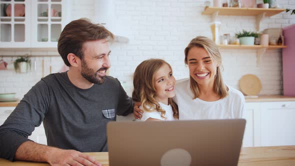 Portrait of Happy Positive Family Young Using Laptop Computer for a Video Call in the Kitchen and