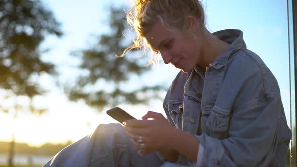 Closeup of Dreamy Gentle and Feminine Blonde Girl with Bun Sitting in Park During Sunset Holding