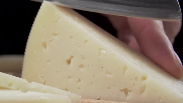 Chef cuts the hard cheese with a knife on a wooden cutting board