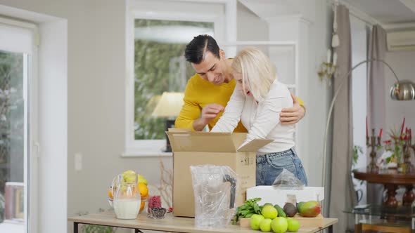 Smiling Middle Eastern Husband Hugging Excited Happy Caucasian Wife Unpacking New Blender at Home in