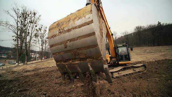 Close-up of a Excavator Bucket That Throws Out the Earth. Slow Motion of a Digger Digging a Pit and