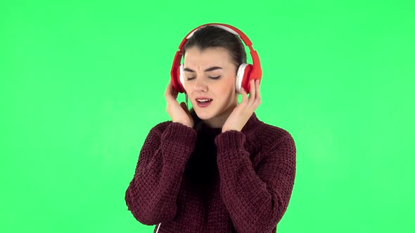 Cheerful Girl Dancing and Enjoys Music in Big Red Headphones. Green Screen