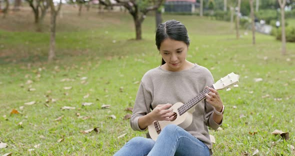 Asian Woman enjoy play ukulele and song in the park