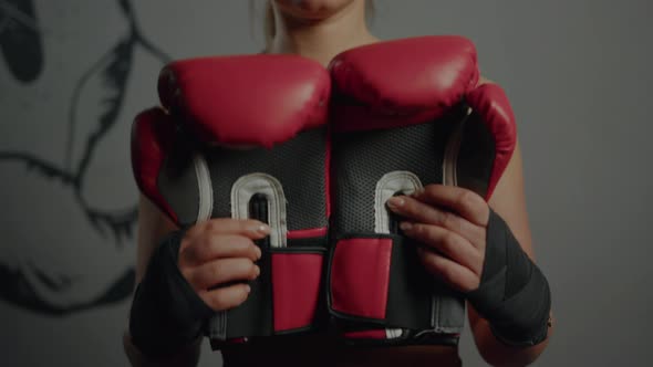 A sporty woman in a tracksuit shows boxing gloves to the camera