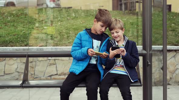 Two Boys Are Sitting At The Bus Stop.