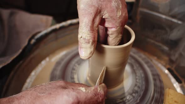 Potter man creates ceramic mug with hands and tool from clay in workshop, closeup. Artisan makes pro