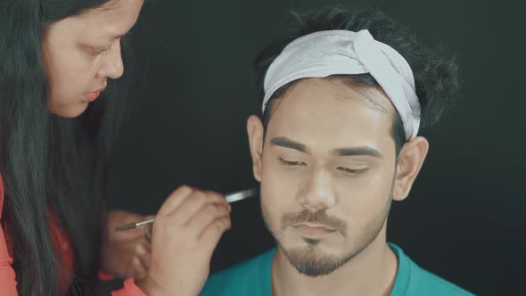 Close up of man's face and make up artist fixing and coloring his beard to be perfect