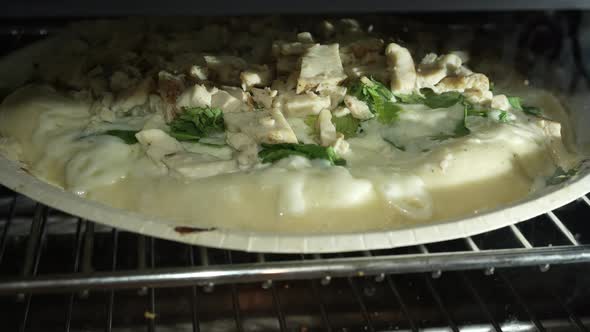 Chicken alfredo pizza with spinach bubbling and cooking in the oven - time lapse