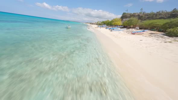 First person aerial racing drone pov over sandy beach with tourists and turquoise sea of Cabo Rojo i