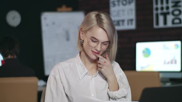 Thoughtful Business Woman Reading Document on Laptop in Dark Office.