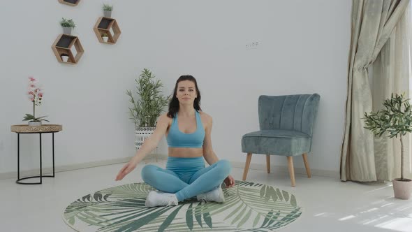 Pretty calm brunette woman in blue sportswear doing practice hand stretching at home