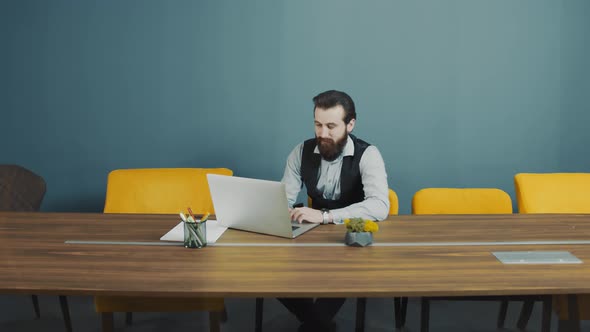 Young Bearded Man Programmer Caucasian Appearance Sitting and Working on a Laptop