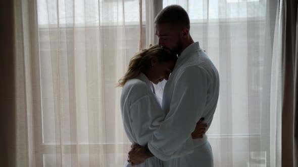 a Man and a Woman in White Coats Hugged and are Standing at a Large Window