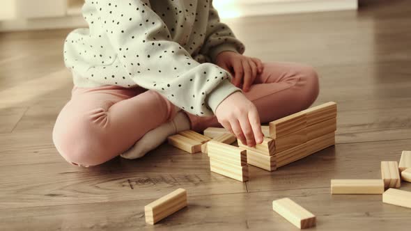 Little child plays a board game, kid builds from wooden bricks blocks.