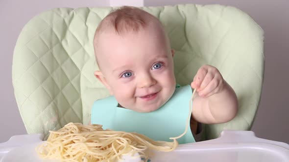 a Little Boy Touches Spaghetti with His Hands While Sitting in a Child's Chair