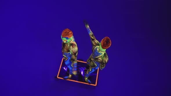 Twin Acrobats Perform A Handstand, Arching Back.Neon Ultraviolet Costumes In An Alien Style