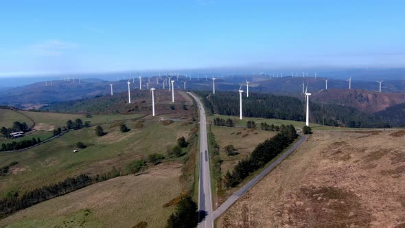 Drone shot traveling forward on a road passing between a wind turbine park in the mountains, sunny d