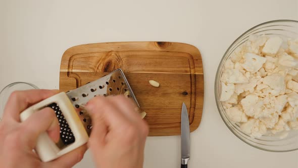 Top view of woman hands grate garlic for salad on a wooden board